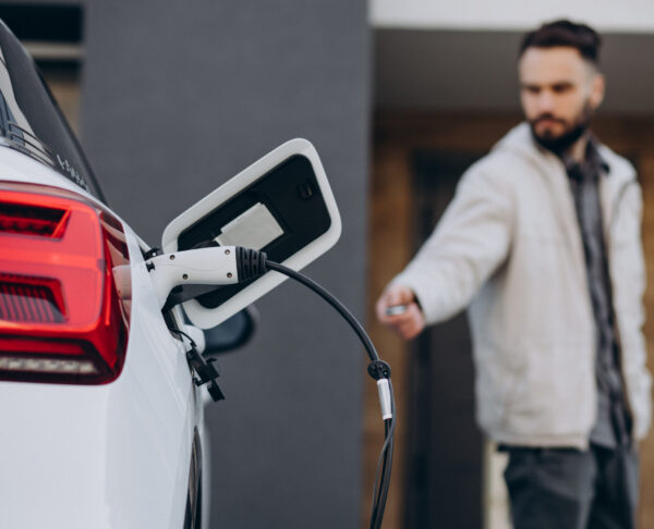 Man charging electric car by the house